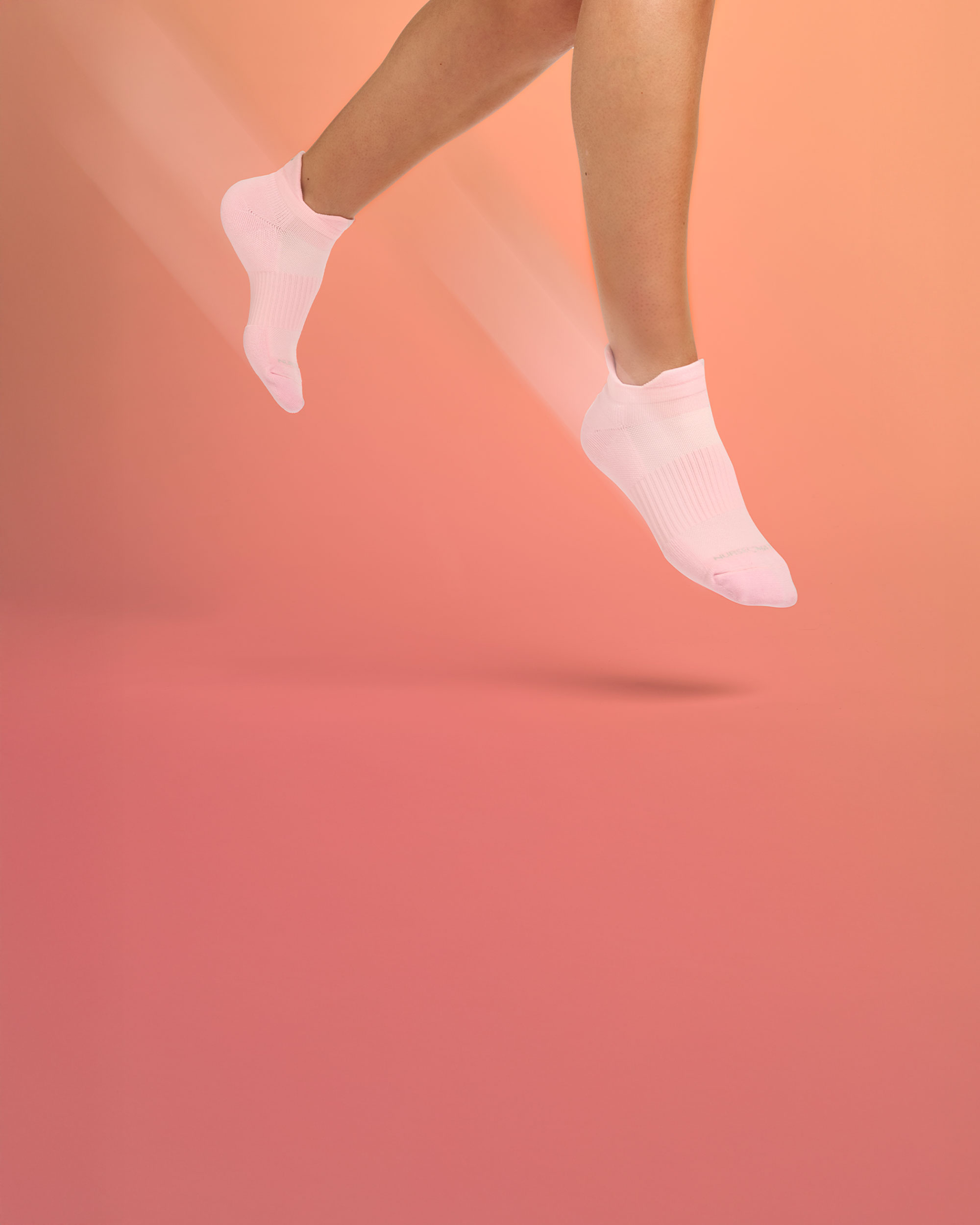 Woman jumping, wearing the Active Stride Anklets on foot in Pink.