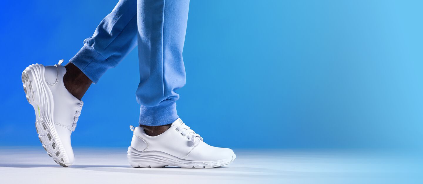 Align Velocity sneaker in white on foot, on a blue background. Back foot is in the air slightly, with toe touching the ground. Front foot is flat on the ground.
