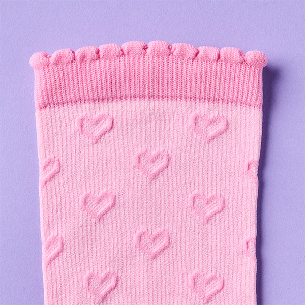 Primer plano de los calcetines de compresión de corazón festoneado en rosa sobre un fondo morado. Compra este calcetín en rosa.
