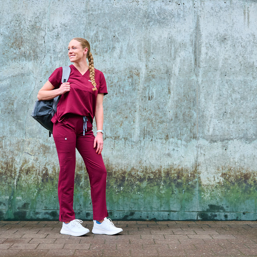 Ella is standing with the Ultimate Nursing Backpack on her shoulder, wearing the Align&trade; Tulia in white on her feet.